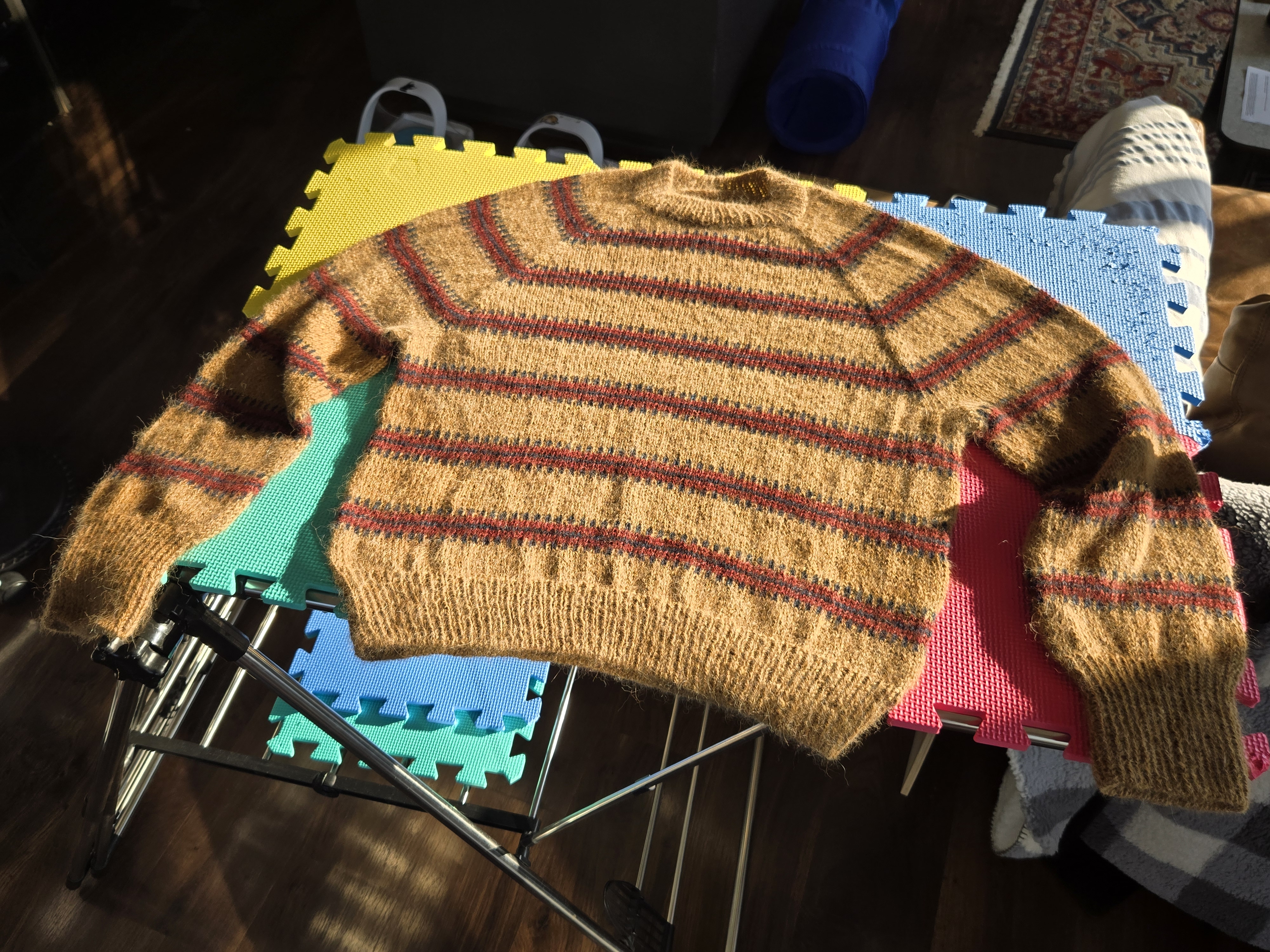 Completed sweater, knit in alpaca with a tan base and stripes from top to bottom of blue and red