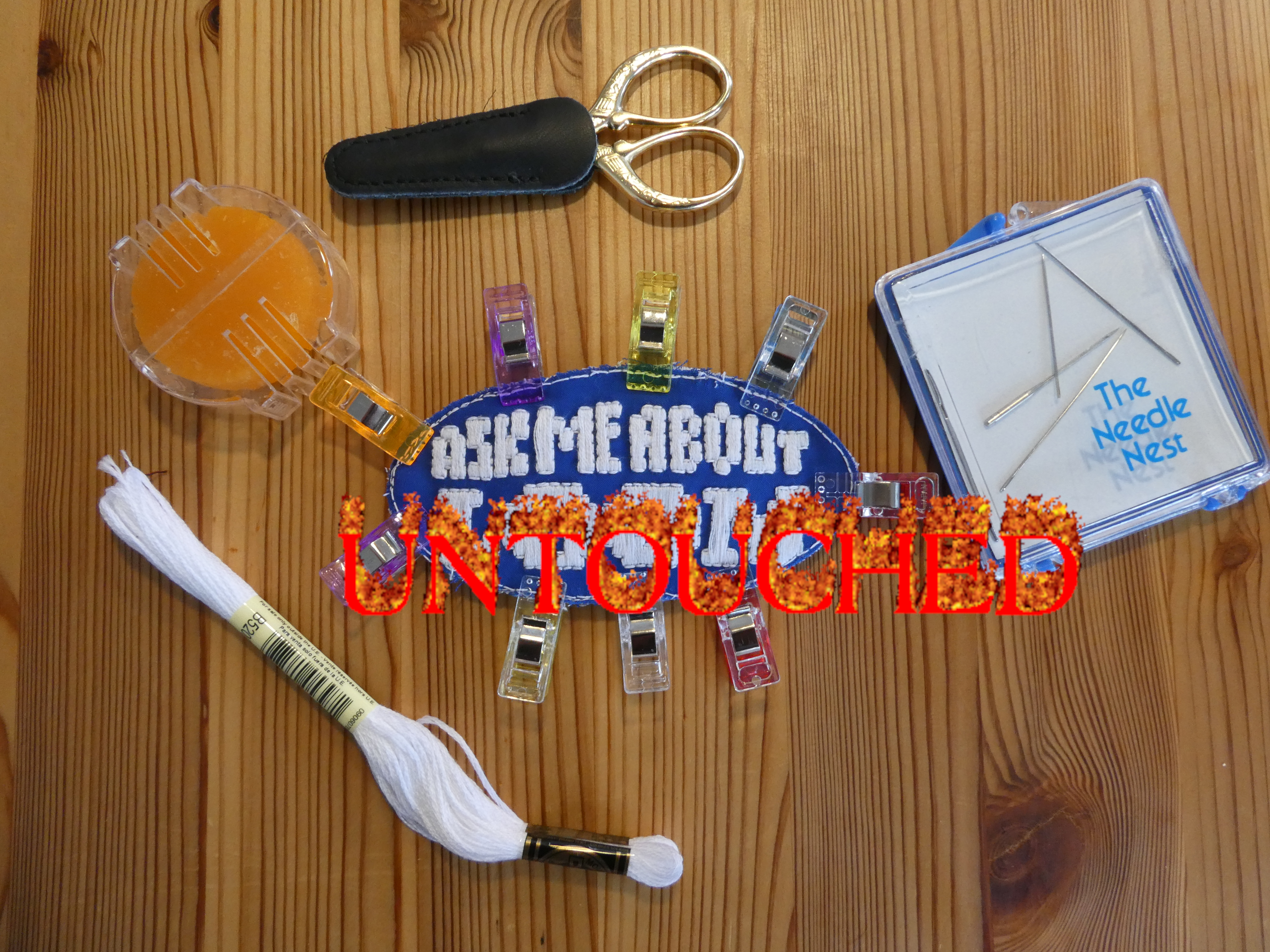 a patch on a blue background that says 'ask me about LOOM' with various embroidery supplies around it (UNTOUCHED)