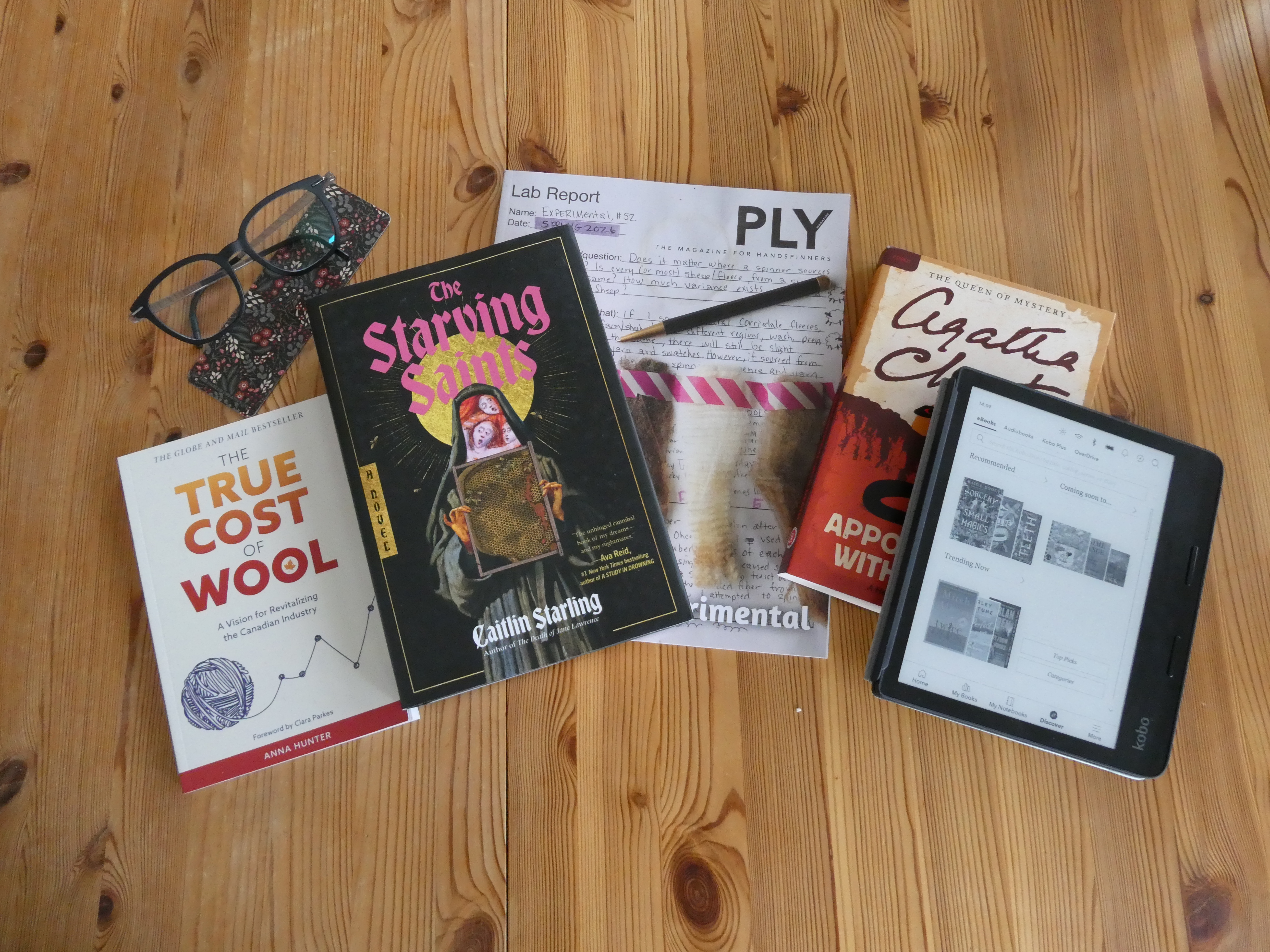books from left to right: the true cost of wool, the starving saints, 52nd edition of ply magazine, appointment with death by agatha christie, my kobo
